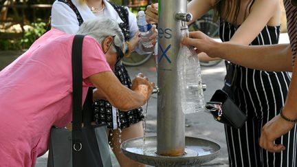 Quatre personnes remplissent des bouteilles depuis une fontaine d'eau potable, à Montpellier (Hérault), le 17 juin 2022.&nbsp; (MAXPPP)