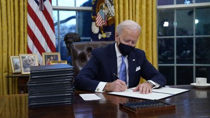 Le président américain Joe Biden signe ses premiers décrets dans le bureau oval de la Maison blanche, à Washington (Etats-Unis), le 20 janvier 2021. (EVAN VUCCI / AP)