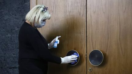 Une employée désinfecte une poignée de porte au théâtre Taganka de Moscou (Russie), le 17 mars 2020. (ANTON NOVODEREZHKIN/TASS/SIPA US/SIPA / SIPA USA)