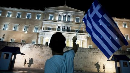 Un homme brandit un drapeau grec devant le Parlement &agrave; Ath&egrave;nes (Gr&egrave;ce), le 5 juillet 2015. (IAKOVOS HATZISTAVROU / AFP)