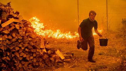 Un habitant tente de sauver sa maison des flammes à Clearlake Oaks, en Californie (Etats-Unis), le 4 août 2018.&nbsp; (NOAH BERGER / AFP)