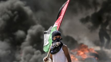 Un garçon porte le drapeau palestinien pendant les affrontements entre les forces israéliennes et les manifestants palestiniens, à la frontière entre la bande de Gaza et Israël. (MAHMUD HAMS / AFP)