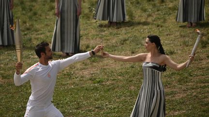 La grande prêtresse transmet la flamme olympique au Grec Stefanos Ntouskos, champion d'aviron aux JO de Tokyo 2020 et premier relayeur. (ANGELOS TZORTZINIS / AFP)