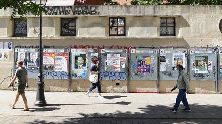 Des passants devant des affiches électorales à côté d'un bureau de vote à Paris, lors du premier tour des élections régionales. (Illustration, le 20 juin 2021). (LUCAS BARIOULET / AFP)