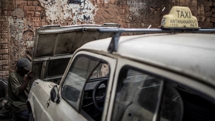 Riri, chauffeur de taxi,&nbsp;répare lui_même sa voiture. Sur son enseigne, un N d'Antananarivo a pris la poudre d'escampette. Mais sa 4L, qui date de 1975, "c'est du costaud".&nbsp; (MARCO LONGARI / AFP)