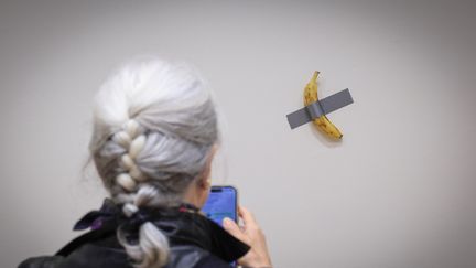 Un journaliste prend une photo de la banane scotchée de l'artiste visuel italien Maurizio Cattelan intitulée "Comedian", exposée lors d'une avant-première médiatique chez Sotheby's à New York, le 8 novembre 2024. (KENA BETANCUR / AFP)