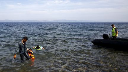 Un Syrien aide son enfant &agrave; s'approcher du rivage en arrivant sur la plage de l'&icirc;le grecque de Lesbos, sous les yeux d'un garde-c&ocirc;te turc, le 26 septembre 2015. (YANNIS BEHRAKIS / REUTERS)