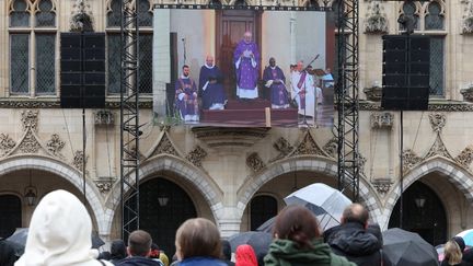 Des personnes rassemblées devant la cathédrale d'Arras (Pas-de-Calais), le 19 octobre 2023, regardent sur un grand écran les obsèques de Dominique Bernard, enseignant tué par un terroriste. (DENIS CHARLET / AFP)