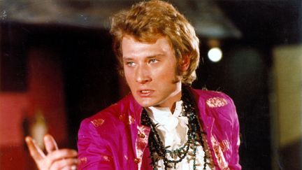 Habillé d'une chemise à jabot et d'une veste rose, Johnny Hallyday joue dans le film "A tout casser", sorti en 1968. (CCFC / CFPF / FINISTERE FILMS / ARCHIVES DU 7EME ART)