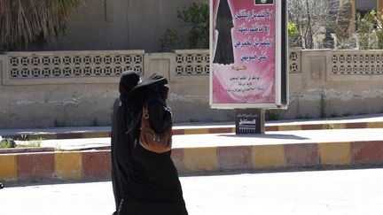 A Raqqa (Syrie),&nbsp;le 31 mars 2014,&nbsp;des femmes int&eacute;gralement voil&eacute;es passent devant un panneau publicitaire sur lequel est affich&eacute; la loi de l'Etat islamique. (REUTERS)