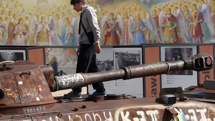 Un jeune homme marche sur un tank russe détruit sur la place Mykhailivska à Kiev le 1er octobre 2024. Photo d'illustration (ANATOLII STEPANOV / AFP)