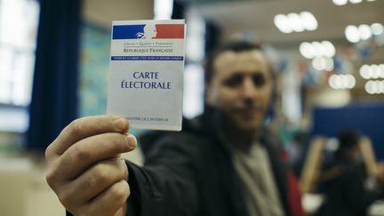 Un homme brandit sa carte d'électeur lors du second tour de l'élection présidentielle, dans un bureau de vote du 20e arrondissement de Paris, le 7 mai 2017. (DENIS MEYER / HANS LUCAS / AFP)