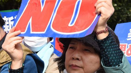 Une femme affiche son opposition à la construction d'une nouvelle base militaire américaine à Okinawa lors d'une manifestation devant la Diète (Parlement) à Tokyo, le 21 février 2016. Plusieurs centaines de personnes ont pris part à cette manifestation dénonçant le plan du gouvernement de laisser construire une base aérienne américaine en remplacement de celle de Futenma existant située dans une zone très peuplée. Les manifestations contre les bases d'Okinawa sont régulières au Japon. (TORU YAMANAKA / AFP)