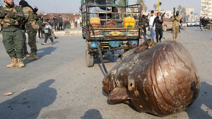 Un camion traine au sol le visage d'une statue à l'effigie de l'ancien président syrien Hafez al-Assad, qui a dirigé le pays depuis 1971 jusqu'à sa mort en 2000, dans les rues de Hama, le 6 décembre 2024. (MUHAMMAD HAJ KADOUR / AFP)