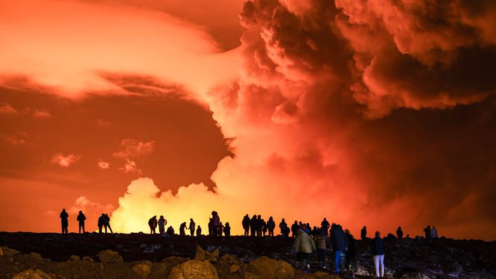 People gather to watch molten lava flow from a fissure on the Reykjanes peninsula, north of the evacuated town of Grindavik (Iceland), March 16, 2024. (AEL KERMAREC / AFP)