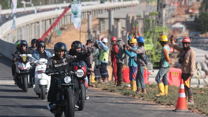 Le président indonésien, Joko Widodo, salue les ouvriers alors qu'il roule à moto sur la nouvelle autoroute menant à la future capitale du pays, Nusantara, sur l'île de Bornéo, le 28 juillet 2024. (ADI WEDA / EPA / MAXPPP)