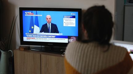 Une enseignante regarde à la télévision le ministre de l'Education nationale,&nbsp;Jean-Michel Blanquer, annoncer que le bac 2020 se fera entièrement en contrôle continu, le 3 avril 2020 à Paris. (ADNAN FARZAT / NURPHOTO / AFP)