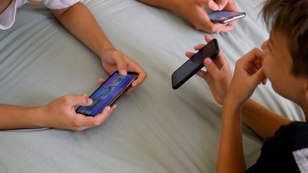 Des adolescents utilisent leurs smartphones, le 27 juin 2022, à Marseille (Bouches-du-Rhône). (NICOLAS TUCAT / AFP)