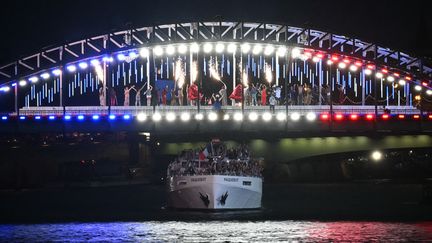 Du bleu, du blanc et du rouge. Le bateau de la délégation française ferme la marche sur la Seine et passe sous la passerelle Debilly, dont le tableau artistique a fait polémique lors de la cérémonie d'ouverture des Jeux olympiques, le 26 juillet. Sous la pluie, rien n'empêchera pourtant les athlètes français de fêter l'ouverture de "leurs" JO, à domicile. (PAUL ELLIS / AFP)