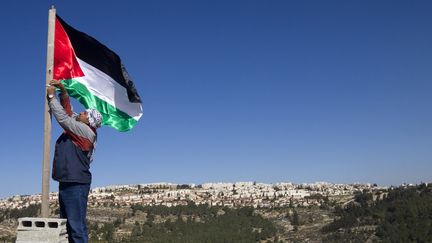 Un Palestinien accroche un drapeau palestinien près d'une colonie israélienne dans le village de Beit Iksa, au nord de Jérusalem, en janvier 2013. (AHMAD GHARABLI / AFP)