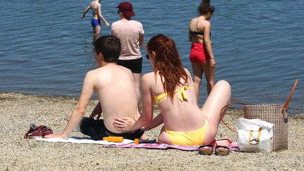 Une jeune femme étale de la crême solaire dans le dos d'un jeune homme&nbsp;sur la plage du plan d'eau de Reiningue, en Alsace, le 2 juin 2019. (VINCENT VOEGTLIN / MAXPPP)