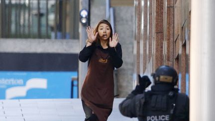 Une otage court en direction d'un policier apr&egrave;s &ecirc;tre sortie du caf&eacute; du centre-ville de Sydney (Australie) o&ugrave; plusieurs personnes sont toujours retenues par un homme arm&eacute;, lundi 15 d&eacute;cembre. (JASON REED / REUTERS)