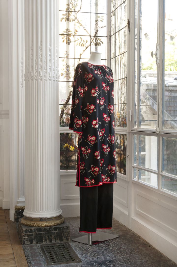 Yves Saint Laurent haute couture, n°39612, printemps-été 1976 : ensemble composé d’une longue tunique en soie imprimée de motifs floraux rouges, blancs sur fond noir, gansée de soie rouge, cotés fendus, et d’un pantalon large en soie noire avec rappel de la ganse. Griffe blanche, graphisme noir. 
 (Cornette de Saint Cyr)