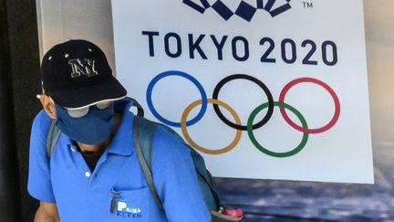 Un homme porte un masque de protection, devant le logo des jeux olympiques de Tokyo 2020. (MLADEN ANTONOV / AFP)