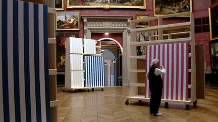 Daniel Buren (debout devant la toile) préparant l'installation de ses "flèches" dans le Grand salon du musée de Picardie
 (France 3 Culturebox)