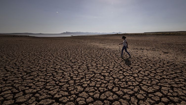 A woman walks on the cracked earth of the al-Massira dam in the village of Ouled Essi Masseoud, 140 kilometers south of Morocco's economic capital, Casablanca, on August 8, 2022. (FADEL SENNA / AFP)