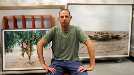 Le photographe israélien Ron Amir pose à côté de son exposition sur les migrants intitulée "Quelque part dans le désert", à Jérusalem, le 30 juillet 2018. (MENAHEM KAHANA / AFP)