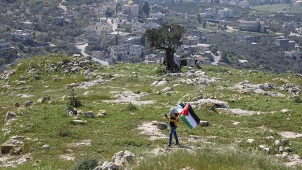 Un personne porte le drapeau de la Palestine près de Naplouse en Cisjordanie, le 29 mars 2021. (JAAFAR ASHTIYEH / AFP)