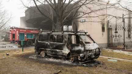 Une camionnette calcinée près d'un bâtiment administratif endommagé dans le centre d'Almaty (Kazakhstan), le 6 janvier 2022, après les violences qui ont éclaté&nbsp;lors de protestations contre la hausse des prix du carburant. (ALEXANDER BOGDANOV / AFP)