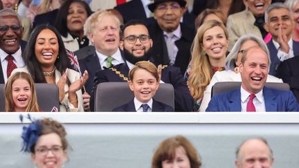 La princesse Charolotte, le prince George et leur père, le prince William, assistent aux concerts de la Platinum Party devant le palais de Buckingham, le 4 juin 2022, à Londres. A l'arrière-plan, le Premier ministre, Boris Johnson. (CHRIS JACKSON / AFP)