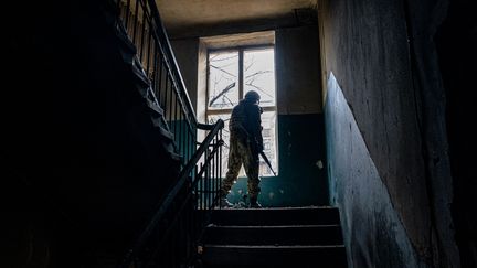 Un soldat ukrainien regarde par la fenêtre d'un immeuble endommagé à Bakhmout (Ukraine), le 27 février 2023. (DIMITAR DILKOFF / AFP)