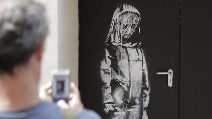 Un homme prend en photo, le 25 juin 2018, "La jeune fille triste" peinte par Banksy près du Bataclan, à Paris, après l'attentat du 13-Novembre. (THOMAS SAMSON / AFP)