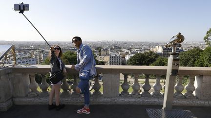 Un couple de touristes se prend en photo au pied de la basilique du Sacré Cœur à Montmartre, le 9 août 2016 (Paris). (PATRICK KOVARIK / AFP)