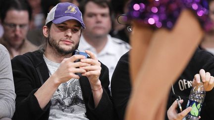 Mais ce n'est rien compar&eacute; &agrave; Ashton Kutcher, au bord du gouffre et du terrain de basket, absorb&eacute; par son iPhone alors que des cheerleaders se d&eacute;hanchent devant lui. Pauvre chou. (LUCY NICHOLSON / REUTERS)