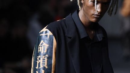 Chez le Japonais Yohji Yamamoto, le vestiaire se déstructure : les vestes se parent de multiples fermetures éclairs, les poches ne tiennent plus qu'à un fil. Les vestes noires, rehaussées par des empiècements rouges ou violets, se portent longues, sur des pantalons ultra-larges et fluides. Des imprimés, dessins ou peintures de femmes nues, fleurs et motifs léopard viennent pimenter d'une touche subversive ces silhouettes.
	 
 (Julien de Rosa/EPA/Newscom/MaxPPP)