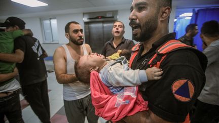 Un membre de la protection civile apporte un bébé blessé à l'hôpital Al-Shifa, à Gaza, après un bombardement de l'armée israélienne, le 11 octobre 2023. (MOHAMED ZAANOUN / MIDDLE EAST IMAGES / AFP)