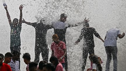 Malgré les dégâts provoqués par les pluies, des habitants de Bombay (Mumbai) tentent de s'amuser de la situation en jouant dans les vagues qui s'abattent sur la promenade Marine Drive, le 9 juillet 2023. (PUNIT PARANJPE / AFP)