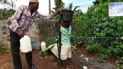 Un homme et un enfant remplissent des seaux d'eau potable, le 27 décembre 2016, à Tsararano (Mayotte). (ORNELLA LAMBERTI / AFP)