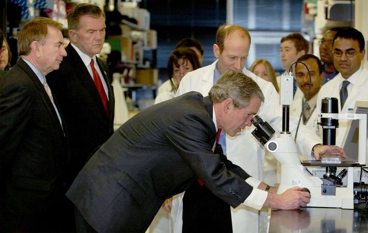 Le pr&eacute;sident am&eacute;ricain George W. Bush observe le virus Ebola au microscope, le 3 f&eacute;vrier 2003, &agrave; Bethesda (Maryland). Nancy Sullivan appara&icirc;t au second plan, au centre. (PABLO MARTINEZ MONSIVAIS/AP/SIPA)