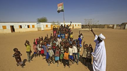 Des enfants soudanais rassemblés sous le drapeau national dans une cour d'école du camp de déplacés d'Otash, à la périphérie de la ville de Nyala, la capitale du Sud-Darfour, le 1er février 2021. (ASHRAF SHAZLY / AFP)