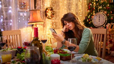 Une femme regarde son téléphone durant un repas de fêtes. Photo d'illustration. (GETTY IMAGES)