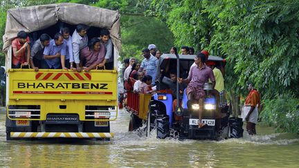 Des personnes victimes d'inondations qui ont trouvé refuge sur un tracteur (à droite) croisent un camion de volontaires qui vont prêter mains fortes aux secouristes à Kainakary dans l'Etat du Kerala en Inde, le 17 août 2018.&nbsp; (TIBIN AUGUSTINE / SIPA)