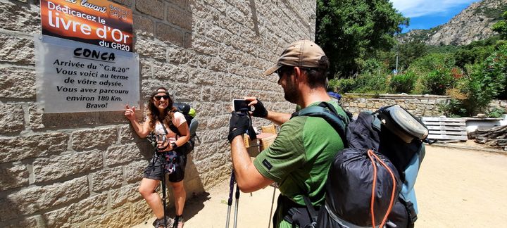 Les randonneurs se prennent en photo devant le petit panneau d'arrivée du GR 20 à Conca (Corse-du-Sud). (BENJAMIN ILLY / FRANCE-INFO)