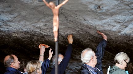 Des pélerins touchent la pierre de la grotte de Massabielle lors de la fête de l'Assomption à Lourdes, le 15 août 2008. (PASCAL PAVANI / AFP)