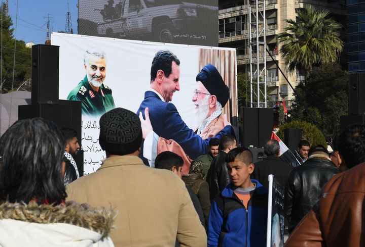 Des manifestants pro-régime à Alep (Syrie), le 7 janvier 2020, devant une affiche montrant le portrait de Qassem Soleimani et Bachar Al-Assad embrassant l'ayatollah Ali Khamenei. (AFP)