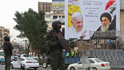 Des gardes de sécurité irakiens se tiennent devant les portraits du pape François et du grand ayatollah Ali Sistani,&nbsp;à Bagdad, le 4 mars 2021, à la veille de la première visite du pape en Irak. (AHMAD AL-RUBAYE / AFP)